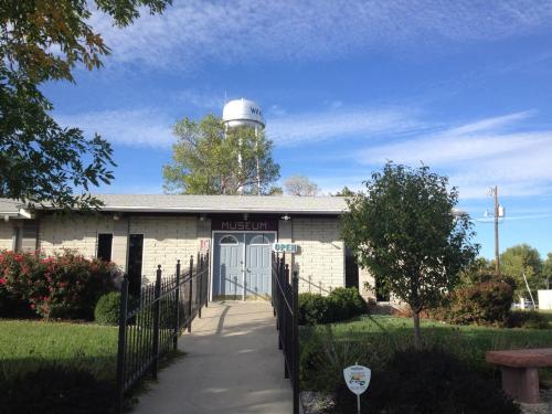 A museum building with a sign reading "OPEN," surrounded by greenery and a water tower in the background under a blue sky.