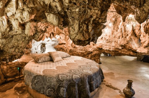 A unique cave bedroom featuring a round bed surrounded by natural rock formations and soft lighting.