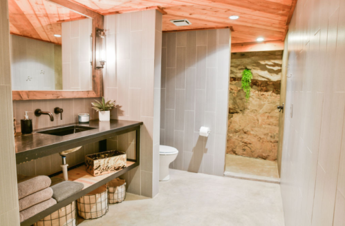 Modern bathroom with a stone wall, wooden accents, a sleek sink, and organized towels in baskets.