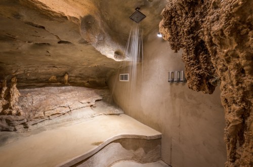 A unique cave-like shower space with a natural rock ceiling and a minimalist design.