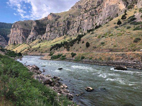 A winding river flows through a rocky canyon, surrounded by lush greenery and steep, rugged cliffs.