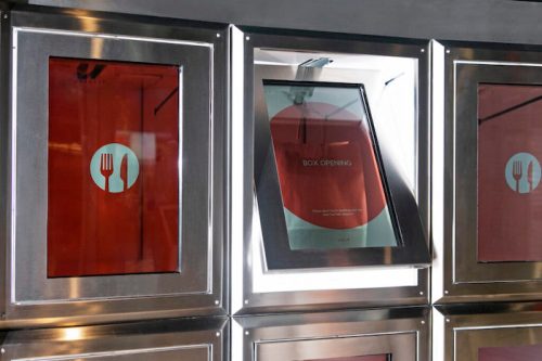 A modern food delivery box with a partially opened window, displaying a menu inside.