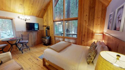 Cozy wooden cabin interior with a bed, dining table, TV, and large windows overlooking a snowy landscape.