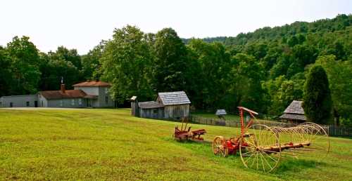 A rural landscape featuring green fields, old wooden buildings, and vintage farming equipment against a backdrop of trees.