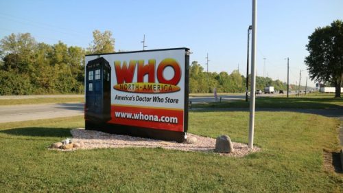 Sign for WHO North America, featuring a TARDIS, advertising "America's Doctor Who Store" along a roadside.