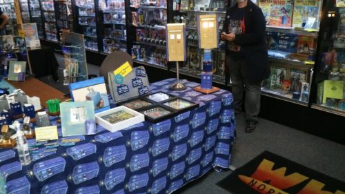 A display table featuring Doctor Who merchandise, including TARDIS models and framed artwork, in a collectibles shop.