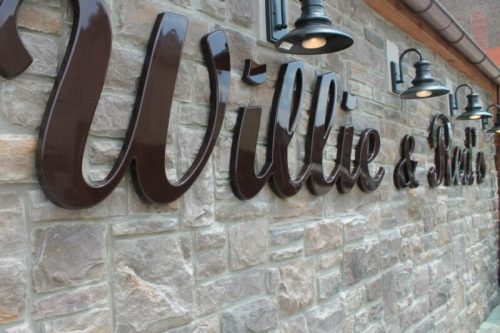 Sign reading "Willie & Ruth's" mounted on a stone wall, illuminated by wall-mounted lights.