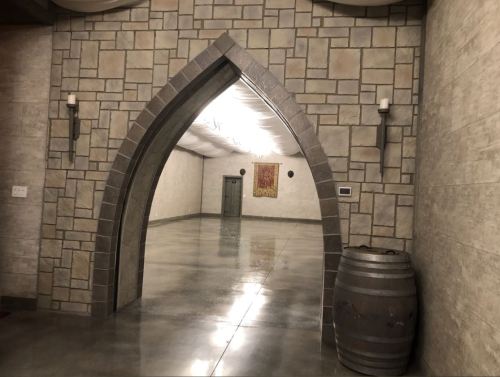 An arched doorway in a stone wall leads to a spacious, empty room with polished concrete floors and a decorative wall hanging.