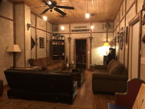 Cozy living room with wooden ceiling, comfortable seating, and warm lighting. Decor includes wall art and plants.