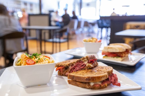 A close-up of a plate with two sandwiches and a bowl of pasta salad in a casual dining setting.