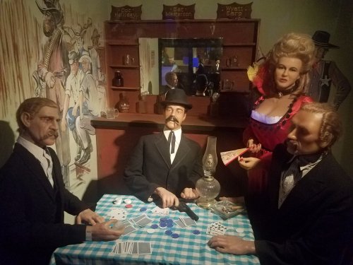 A scene with lifelike figures at a poker table, featuring a woman in a red dress and men in suits, set in a Western theme.