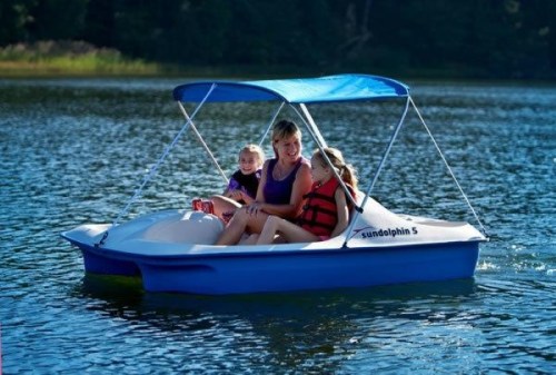 A woman and two children enjoy a sunny day on a blue paddle boat in a calm lake.