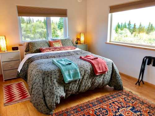Cozy bedroom with a large bed, colorful towels, and windows showcasing a scenic view of trees and nature.
