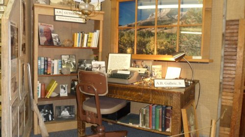 A vintage office setup featuring a wooden desk, typewriter, bookshelves, and framed photos on the wall.