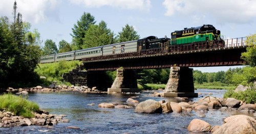 A scenic train in New York crosses a trestle bridge over a river.