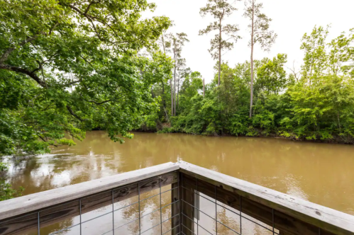 View of a calm river surrounded by lush green trees from a wooden deck.