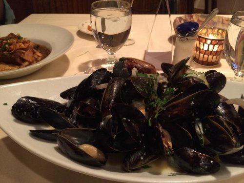 A plate of mussels garnished with herbs, with a glass of water and a candlelit table in the background.