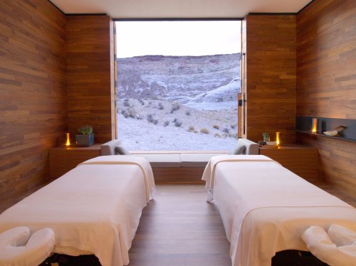 A serene spa room with two massage tables and a large window overlooking a rocky landscape. Soft lighting enhances tranquility.