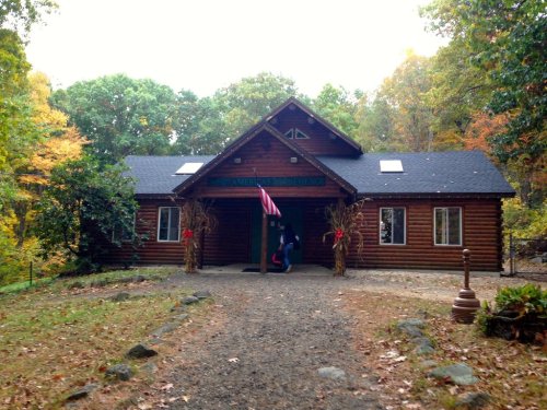 A rustic log cabin surrounded by autumn trees, with a path leading to the entrance and seasonal decorations.