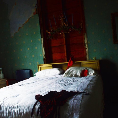 A dimly lit bedroom with a bed, decorative wall, and a red garment draped on the bedspread.