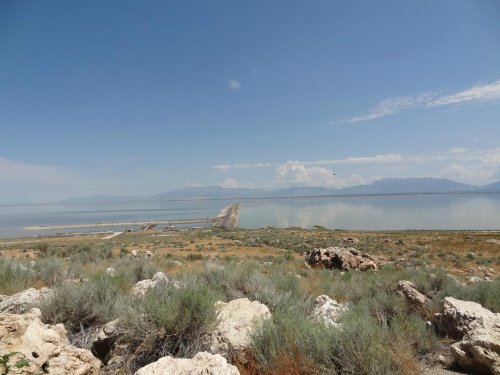 A scenic view of a vast lake surrounded by mountains and rocky terrain under a clear blue sky.