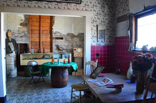 A vintage room with a green table, wooden barrel, and rustic decor, featuring exposed walls and various artifacts.