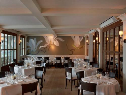 Elegant restaurant interior with white tablecloths, wooden accents, and floral wall art. Soft lighting creates a warm ambiance.