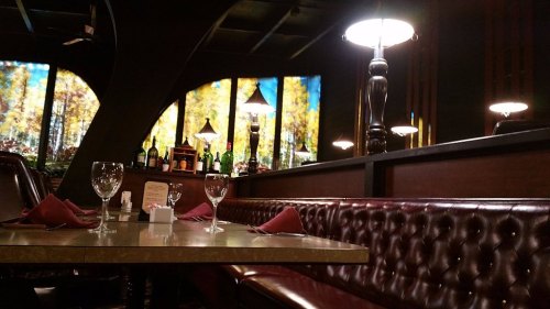 Cozy restaurant interior with a wooden bar, elegant lighting, and a view of autumn trees through large windows.