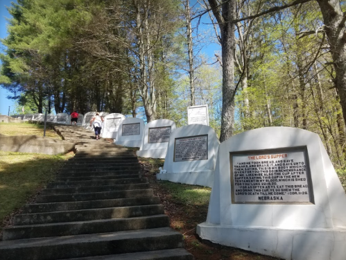 A stone staircase leads up a hill lined with memorials and plaques under a clear blue sky and trees.