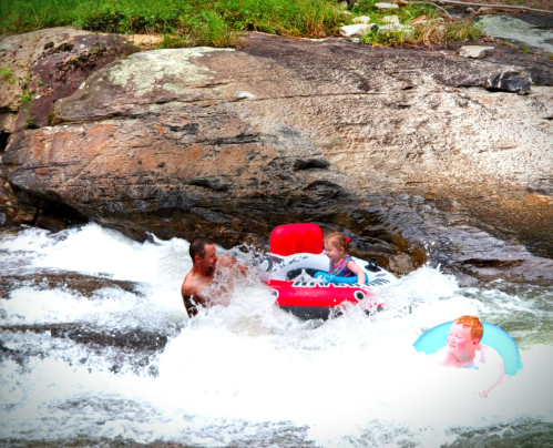 A man and two children play in a rocky stream, enjoying inflatable floats in the rushing water.