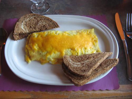 A plate with a cheese omelette and slices of brown bread on the side, set on a table with utensils.