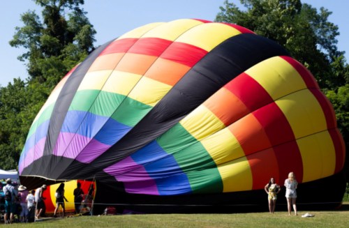 A colorful hot air balloon being inflated, with people gathered around in a sunny park setting.