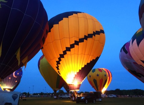 Colorful hot air balloons illuminated at dusk, set against a blue sky.