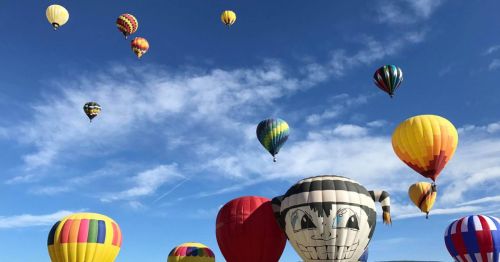 A colorful array of hot air balloons in the sky, including one with a playful face design, against a blue backdrop.
