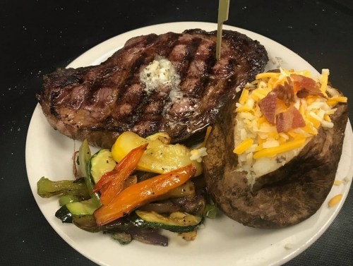 A grilled steak with butter, served with sautéed vegetables and a baked potato topped with cheese and bacon.
