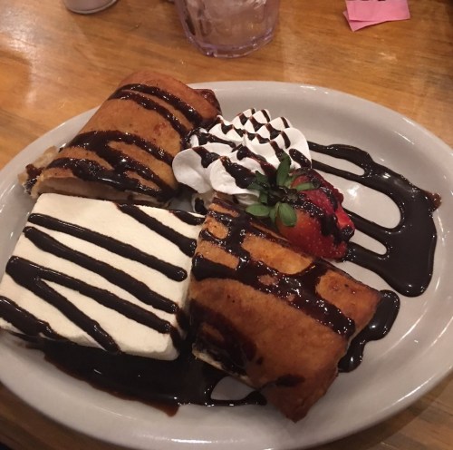 A plate of dessert featuring chocolate-drizzled fried pastries, whipped cream, and a strawberry.