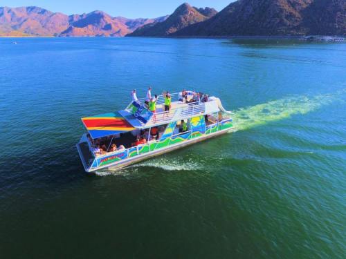 A colorful boat with passengers sails on a calm lake surrounded by mountains under a clear blue sky.