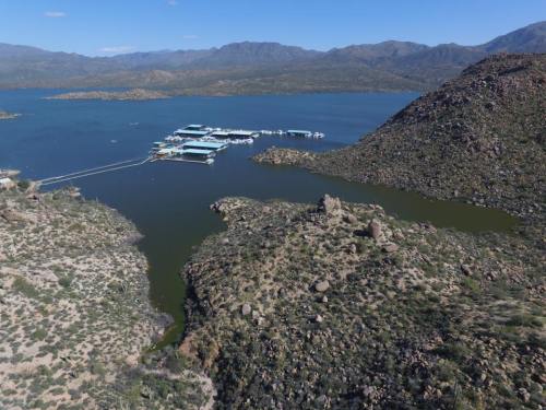 Aerial view of a lake surrounded by rocky hills and mountains, with a marina docked on the water.