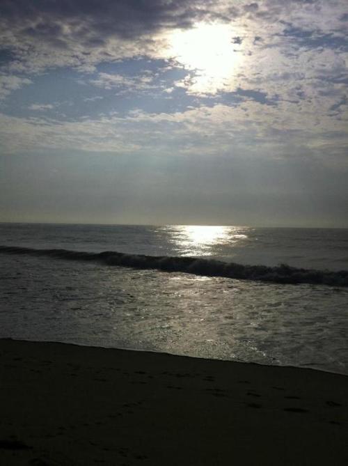 A serene beach scene at sunset, with gentle waves and a cloudy sky reflecting sunlight on the water.