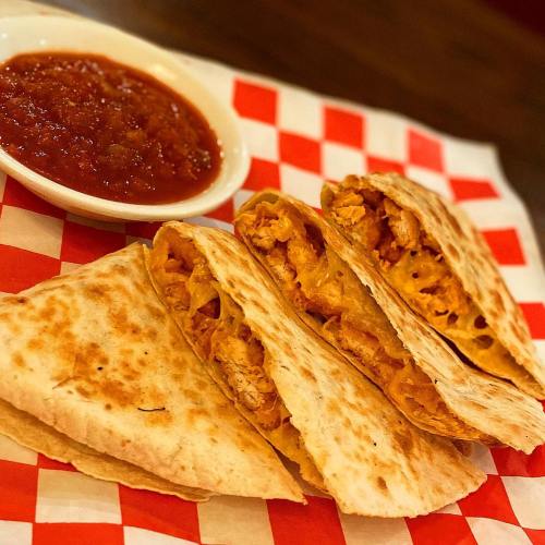 Three quesadillas filled with chicken, served with a side of salsa on a red and white checkered plate.