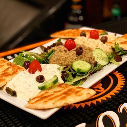 A platter of hummus, tzatziki, and salad garnished with cherry tomatoes, olives, and pita bread.