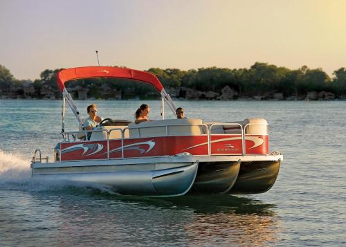 A pontoon boat with three people enjoying a ride on a calm lake during sunset.