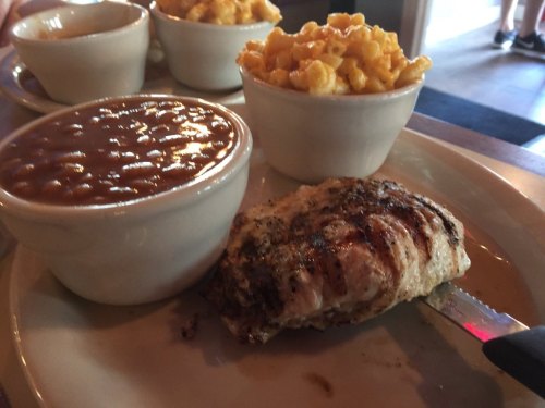 Grilled chicken breast with sides of baked beans and macaroni and cheese in white bowls.