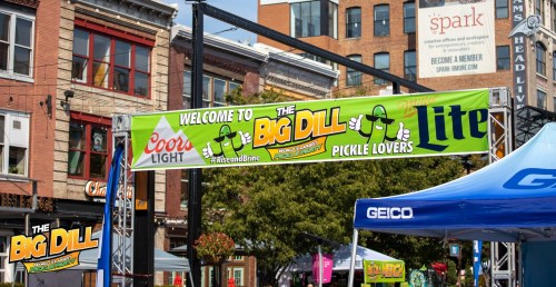 Banner for "The Big Dill" pickle festival, featuring cartoon pickle characters and sponsors like Coors Light and Miller Lite.