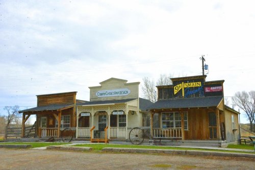 A rustic storefront with wooden facades, featuring signs for a design shop and a coffee shop, set against a cloudy sky.