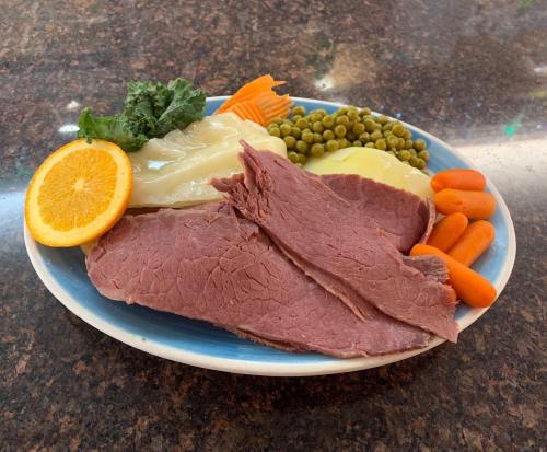 A plate of sliced corned beef with cabbage, carrots, peas, and an orange slice, arranged on a blue rimmed dish.