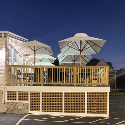A wooden deck with white umbrellas at dusk, surrounded by a parking lot and a building in the background.