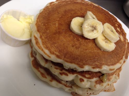 Two fluffy pancakes topped with banana slices, served with a side of butter in a small cup.