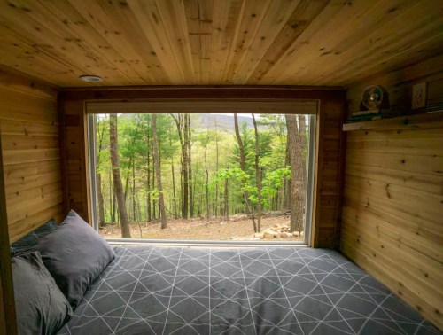 Cozy bedroom with a large window overlooking a forested landscape and mountains in the distance.