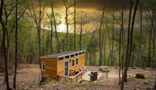 A cozy wooden cabin nestled in a forest, surrounded by trees and a scenic view under a dramatic sky.